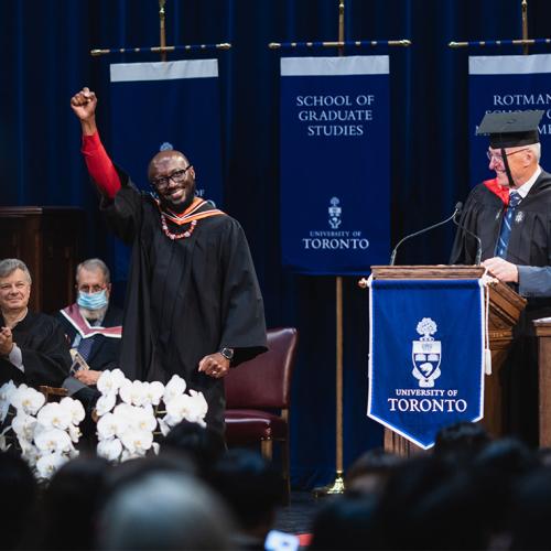 A smiling graduate pumps his fist on the stage at Rotman, while other officials look on