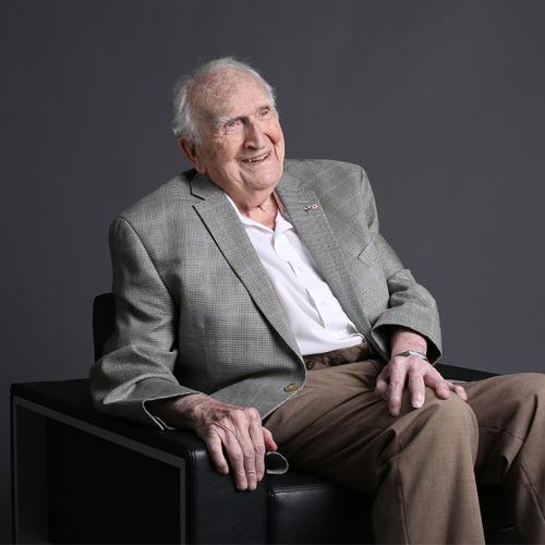 Lou Siminovitch sitting in an armchair and laughing.