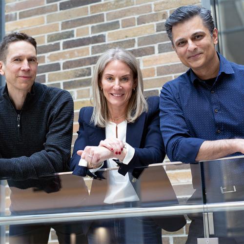 Tomi Poutanen, Mara Lederman and Muhammad Mamdani smile and lean on a balcony railing together.