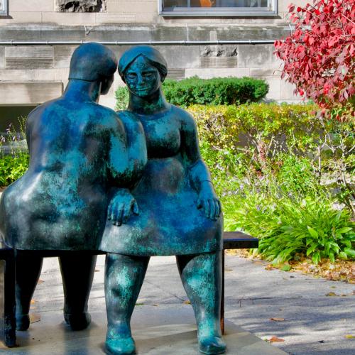 In the garden at St. Michael's College, a metal sculpture depicts two women on a bench chatting together.