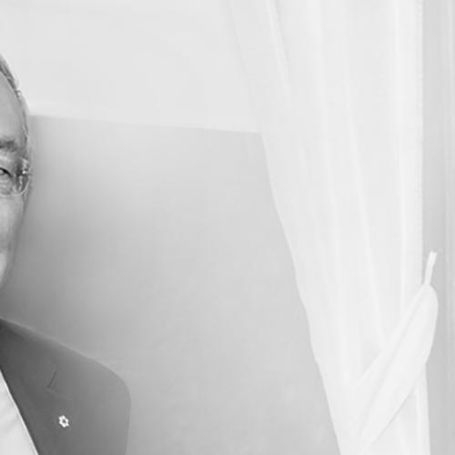 Portrait of Arthur Scace smiling, standing by a curtain indoors.