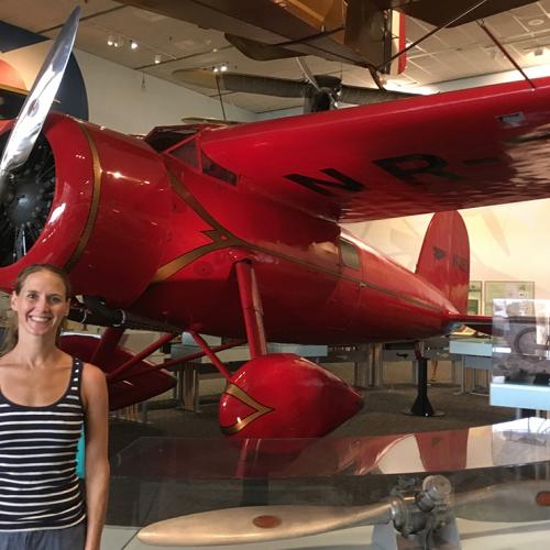 Lindsay Zier-Vogel stands by a small airplane with a single nose-propellor and teardrop-shaped wheel covers.