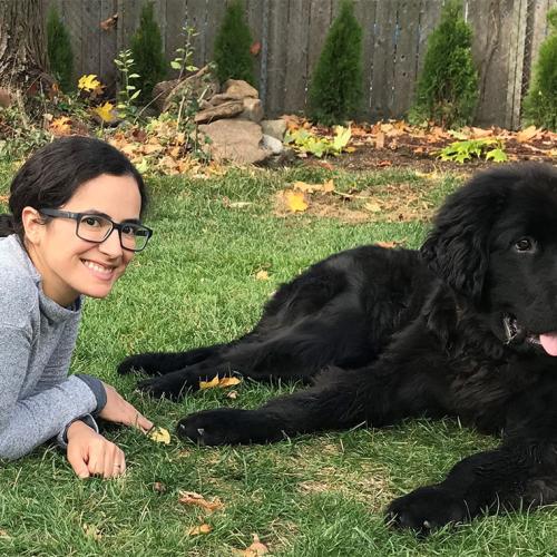 Sofia Bonilla smiles happily as she lies on a grass lawn with her very large Newfoundland dog, Snuffie.