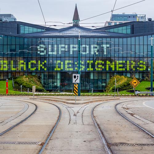 The words Support Black Designers are spelled out across the glass windows of the modern half of One Spadina.