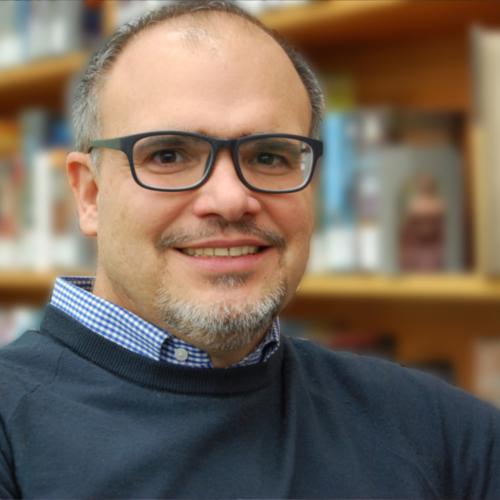 A portrait of Teo Salgado smiling in front of a bookshelf.