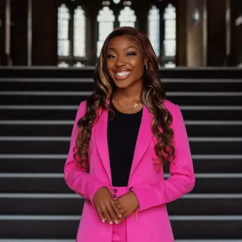 Portrait of Tobi wearing a neon pink suit and standing in front of an old wooden staircase