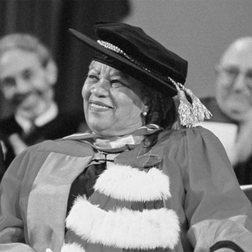 Toni Morrison smiles, wearing academic robes and a hat as she sits on stage at Convocation Hall after receiving an honorary degree