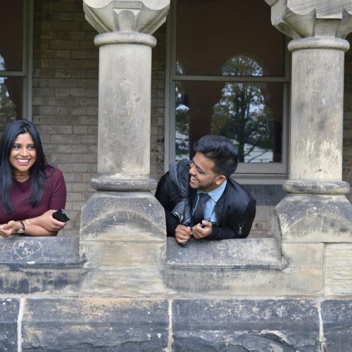 Trina and Kal look at each other playfully, standing in a stone building