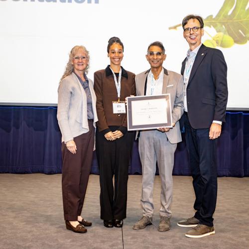 Dr. Vivian Rambihar accepts his award on stage from three other people, Carl Mitchell's wife Margaret Shaw, daughter Nancy Mitchell and UTAA President Corwin Cambray.