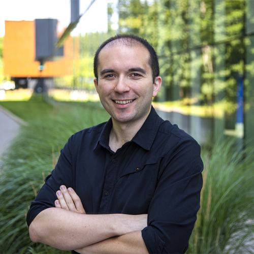 Florian Shkurti stands with arms folded on the grass outside a building.