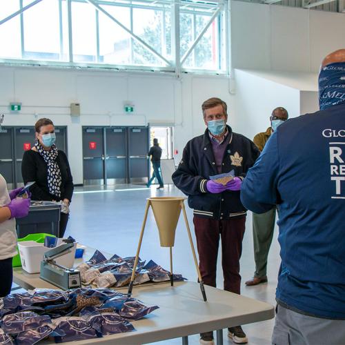 Mayor John Tory, wearing a mask and gloves, listens to a man wearing a hoodie with the words GlobalMedic on it.