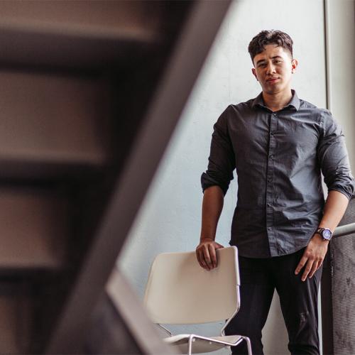 Christian Cordero looks serious as he stands near a bright window under a staircase.