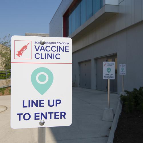 Signs outside Highland Hall read: Scarborough COVID-19 vaccine clinic, line up to enter.