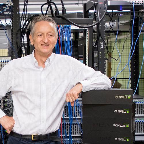 Geoffrey Hinton standing in a technology lab, smiling