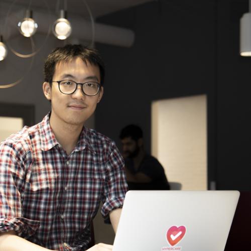 Albert Tai smiles as he looks up from a laptop with the Hypercare logo on its back.