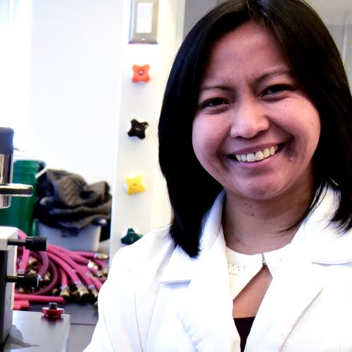 Ruby Sullan smiles while standing in a lab with taps and tubes on the walls.