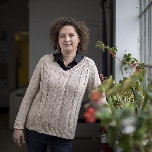 Shannon Simpson looks thoughtful as she stands by a window, the sill lined with potted plants.