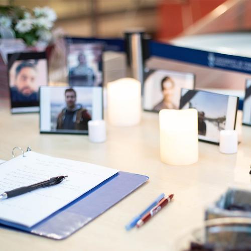 A book of condolence lies open on a table covered with candles and student photographs.