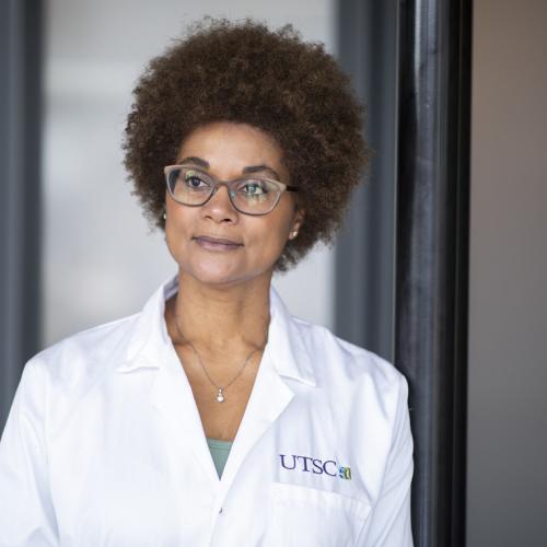 Maydianne Andrade looks serious, standing in a hallway wearing a lab coat with the U of T Scarborough logo.