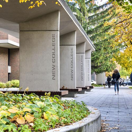 The words New College are engraved in concrete pillars holding up an inviting gateway with benches.
