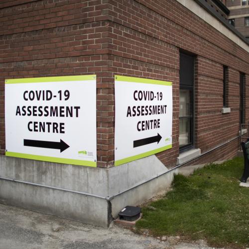 A sign on a brick building reads: COVID-19 Assessment Centre.