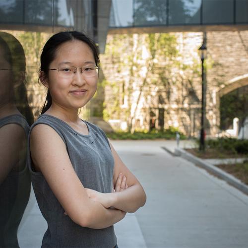 Maddy (Xiaoxiao) Zhang smiles as she leans on a reflecting wall in a sunny courtyard.