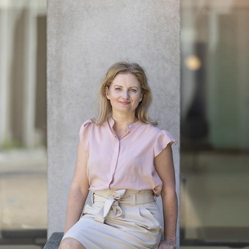 Jennifer Gommerman smiles, sitting in front of a concrete pillar outdoors.