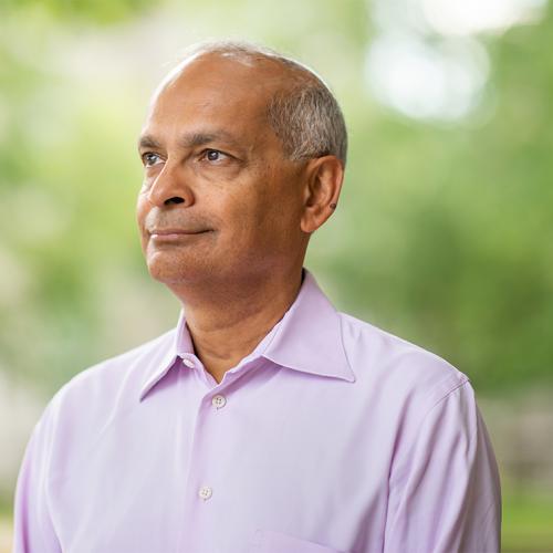 Vivek Goel smiles and looks thoughtful, standing in a park outdoors.