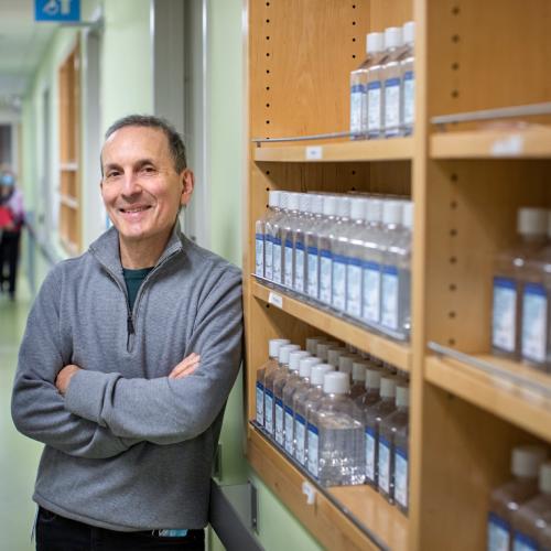 Daniel Druckers smiles and leans on a shelf of labelled bottles.