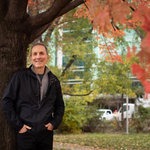 Daniel Drucker smiles as he leans on a tree in full fall colour.