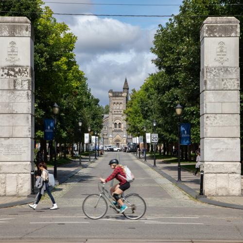 Pedestrians walk past the Alumni Gates on U of T's St. George campus. University College is pictured in the background. 