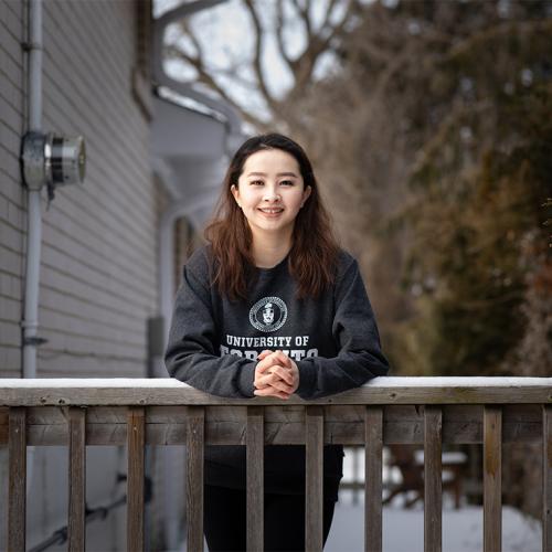 Melody Bagaa smiles as she leans on a snow-covered railing. She wears a University of Toronto sweatshirt.
