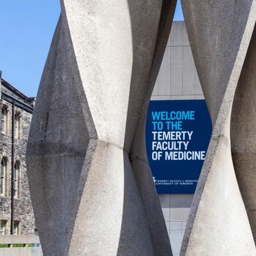 On a sunny day, a sign reading Temerty Faculty of Medicine is framed by an abstract stone sculpture.