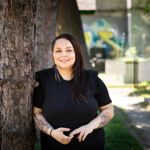 Andrea Johns smiles as she leans on a tree outdoors.