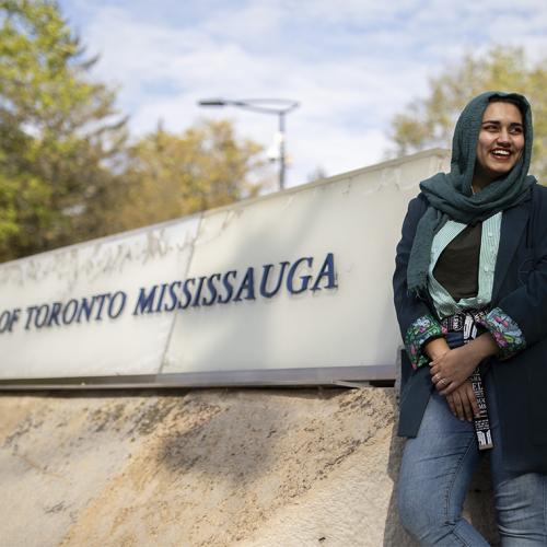 Amna Adnan laughs as she stands next to a large sign that says University of Toronto Mississauga.