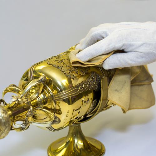 A gloved hand gently dusts the elaborate gold head of U of T's ceremonial mace.