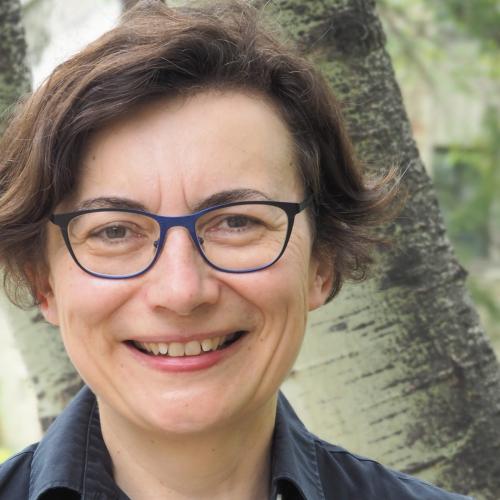 Valerie Korinek smiles while standing in front of a birch tree outdoors.