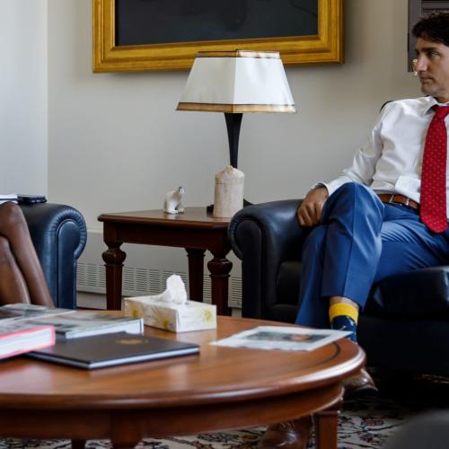 Vandana Fatima Kattar and Justin Trudeau sit in armchairs in an office, next to a table of books and documents.