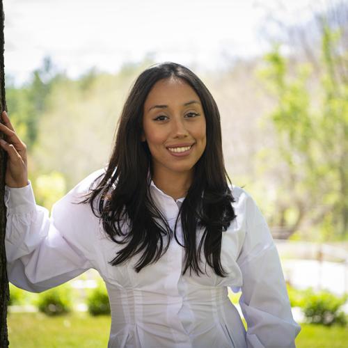 Vanessa Alfaro smiles as she rests her right hand on a tree in a park outside.