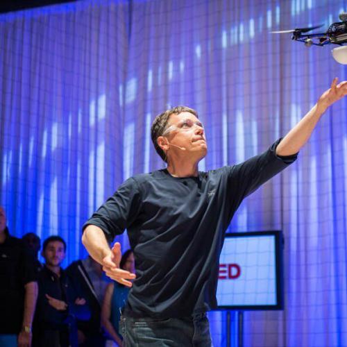 Raffaelo D’Andrea reaches up to a small drone hovering just above his hand.