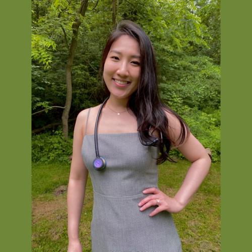 Yukei Ng smiles as she stands in a garden with one hand on her hip.
