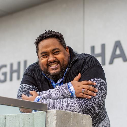 Keon Priestley smiles and laughs as he leans on the railing outside U of T Scarborough's Highland Hall.