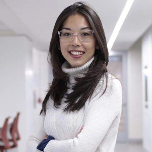 Kimberly Ren smiles with arms folded, standing in a bare indoor office room.