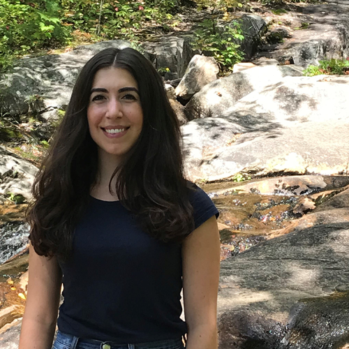 Anastasia Boutziouvis smiles, standing by a rocky stream outdoors.