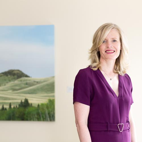 Claire Kennedy smiles as she stands beside a painting of green hills.