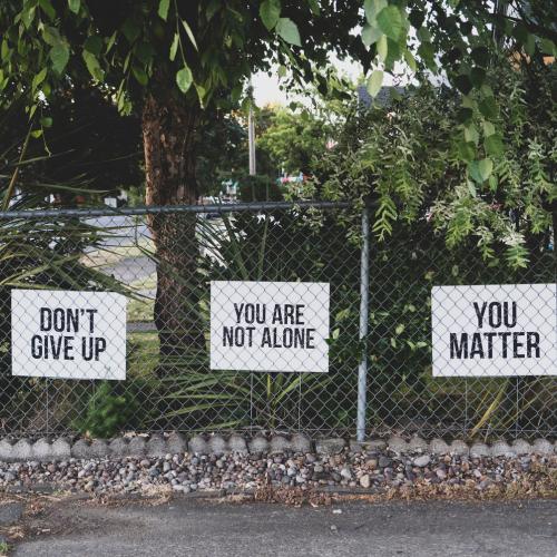 Three signs on a fence read: Don't give up, You are not alone, You matter.