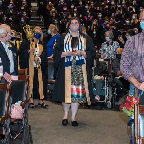 The audience in Convocation Hall stands as Lindsey Fechtig walks down an aisle holding an eagle feather.