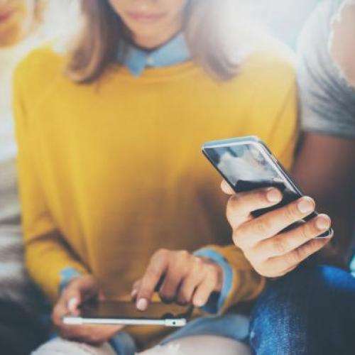 photo by Shutterstock of three students on their phone.