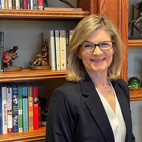 Gretchen Kerr smiles, standing in front of shelves full of books and whimsical carved bookends.