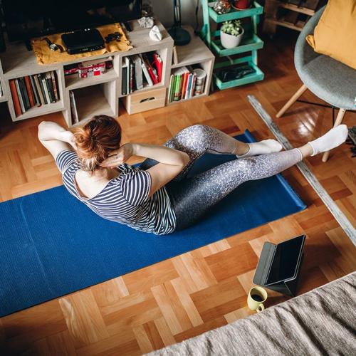 A woman touches her elbow to her knee on a yoga mat on a living room floor.